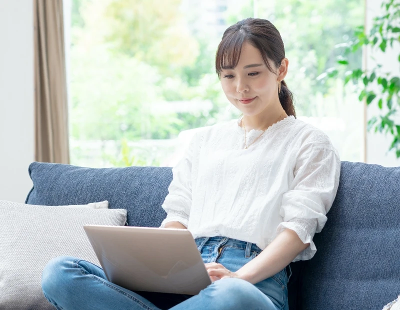 女性が在宅でパソコンを見ながらソファに座っている様子