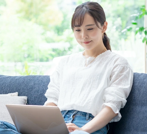 ソファに座り、ノートパソコンを使っている女性の姿