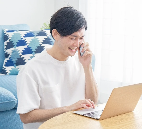 机で男性が、ノートパソコンと携帯電話を使って作業している