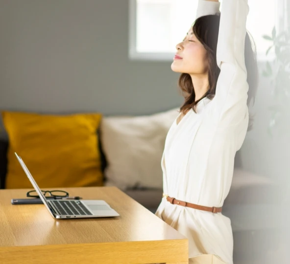 ノートパソコンの前で腕を伸ばしているリラックス女性の姿