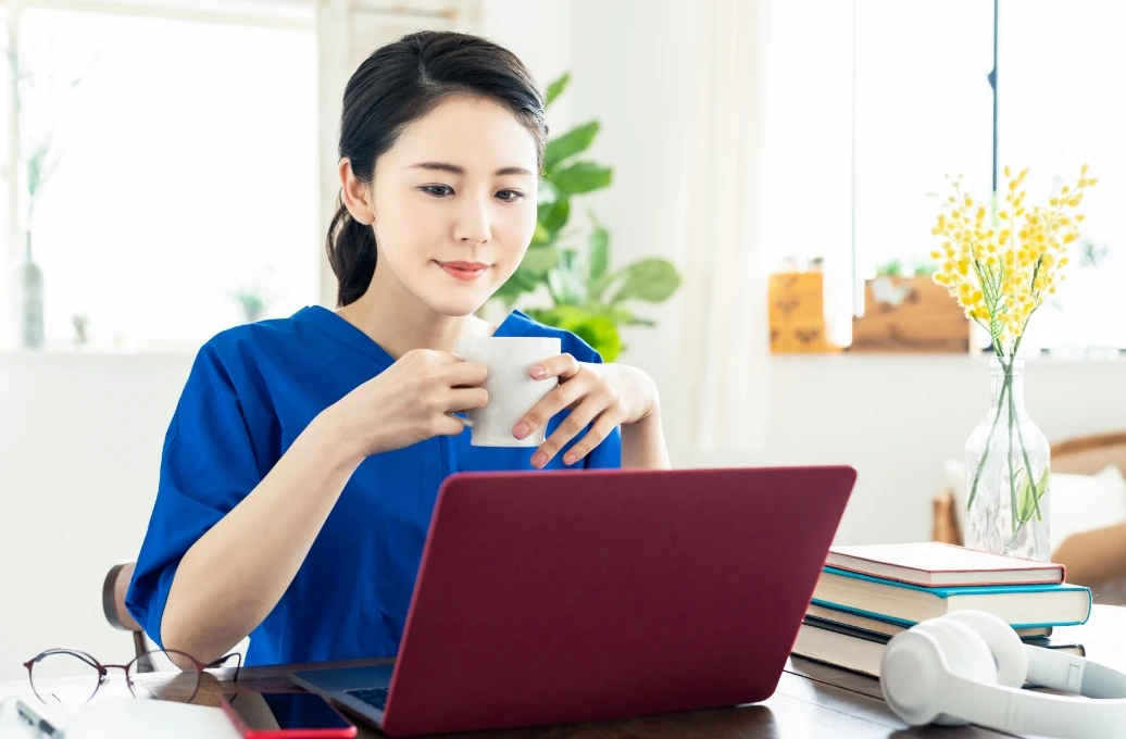 青い服を着た女性が机に座り、ノートパソコンを使っています。